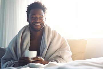 Fototapeta premium Vacation. A middle-aged African American sits on a bed with a mug of aromatic coffee. He smiles and looking at camera.