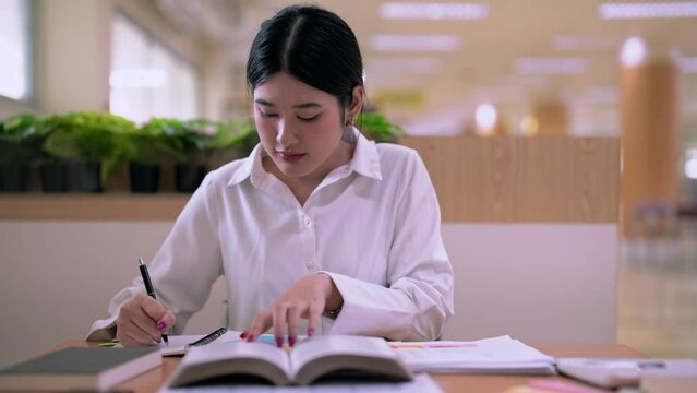 Young Asian Female student college do homework and reading a book for final exam at library, education concept.
