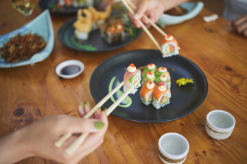 Sushi, hands and eating food with chopsticks at restaurant for nutrition at table. Closeup of people with wooden sticks for dining, Japanese culture and cuisine while sharing with creativity on plate