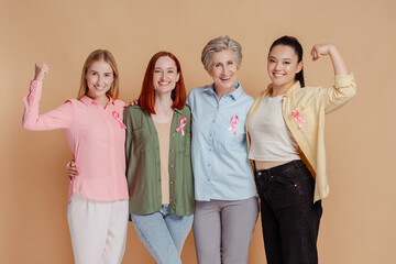 Portrait smiling strong multiethnic women wearing pink ribbon celebrate recovery isolated on beige background. Health care, support. Breast cancer awareness month 