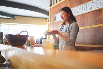 Chinese food, waitress and an asian woman in a sushi restaurant to serve a traditional meal for nutrition. Kitchen, smile and cooking with a happy young employee in an eatery for fine dining cuisine