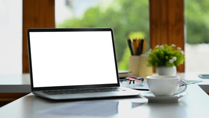 Fototapeta premium Laptop with empty display, coffee cup and office office supplies on white table. Simple workplace.