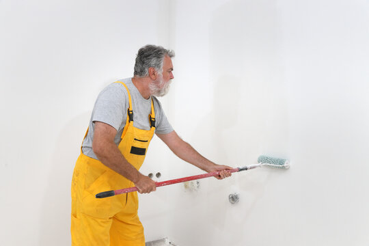 Senior adult caucasian worker painting wall to white with paint roller