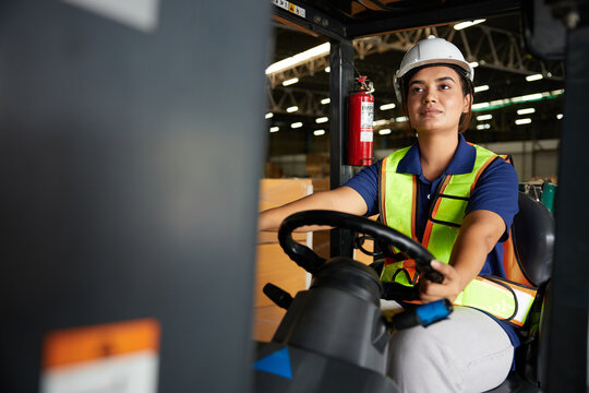 Indian worker driving a forklift and looking to something in warehouse storage
