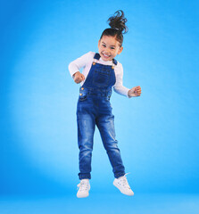 Happy, jumping and portrait of a child in a studio with excitement, joy or wow expression. Happiness, smile and full length of a girl kid model moving for good news isolated by a blue background.