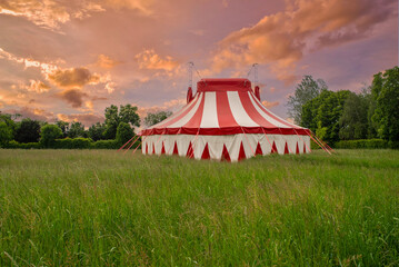 Colourful circus tent on green meadow against a colorful sunset sky