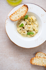 White plate with italian tortellini in brodo, above view on a beige stone background, vertical shot
