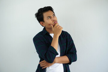 Fototapeta na wymiar young asian man showing thinking pose with hand touching the chin while his eyes looking to the up isolated on white background.