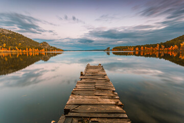 Rustic wooden pier on a blue lake sunset and smooth reflection of the sky in the water. Long...
