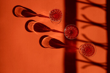 Shadows and fractals of three crystal glasses filled with red liquor being projected on an orange surface.