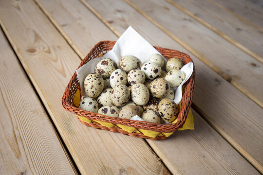 Detalhe ovos de codornizes numa cesta de palha sobre mesa de madeira.