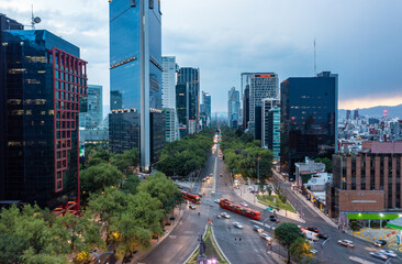 Aerial view of financial skyscrapers with moving bus and car on street during day in Mexico City under cloudy blue sky
