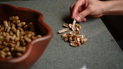 Eating roasted peanut with a bowl of full peanuts.