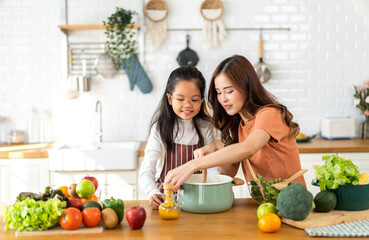 Portrait of enjoy happy love asian family mother with little asian girl daughter child help cooking food healthy eat with fresh vegetable testing smell soup in a pot with spoon.help mommy in kitchen