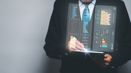 A businessman in a suit sits in his office, analyzing data on a virtual screen of his tablet, symbolizing the concept of using technology to enhance professional work.
