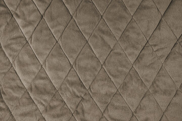 Fototapeta premium Quilted velours fabric background. Brown texture blanket or puffer jacket, stiched with diamond pattern, soft wrinkled surface, crupmed textile