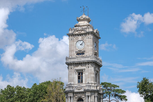 Dolmabahçe Palace clock tower with blue sky background and trees. Open space area.
