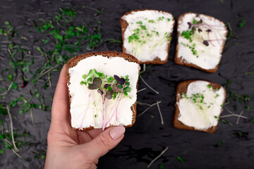 sandwich with cream cheese and microgreens in a woman's hand