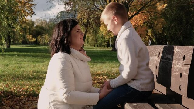 Mother with son on a walk in the autumn park. Woman kissing son and smiling. Horizontal video