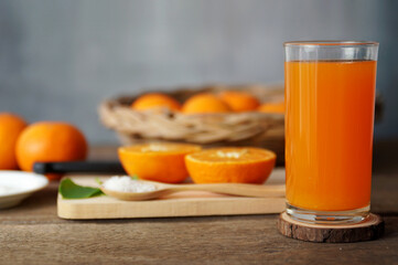 Glass of orange juice Placed on an old wooden table There are equipment and ingredients in the background.