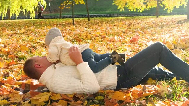 Portrait of a happy family resting in the autumn forest. Dad picks up his son in his arms while lying down on blanket. Horizontal video - Powered by Adobe