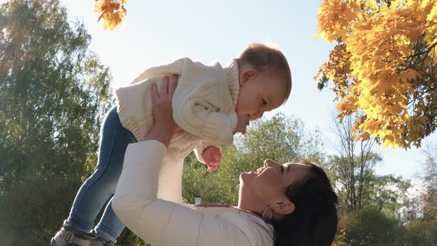 Caucasian young mother playing throwing up in air cute funny adorable toddler boy. Mom and son having fun in autumn fall park with yellow leaves. Family lifestyle activity outdoor. Horizontal video