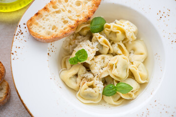 Tortellini in bouillon served with grated parmesan, green basil and ciabatta in a beige plate, close-up, selective focus - obrazy, fototapety, plakaty