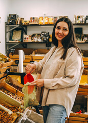 Young woman pouring almonds into  mesh reusable bag at market.