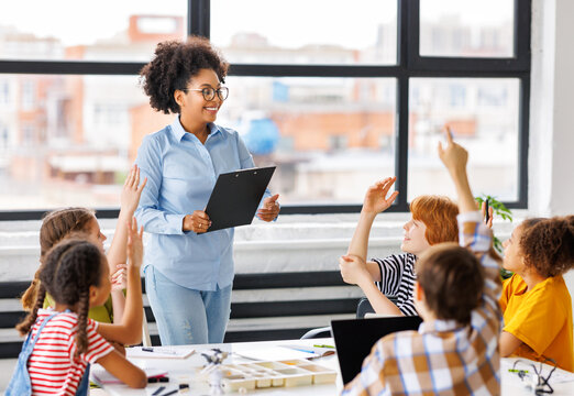 African american teacher smiling and looking at students raising their hand in class during lesson.