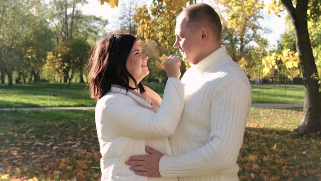 Husband and wife in white warm clothes posing for the camera in the autumn park on a sunny day. Horizontal photo