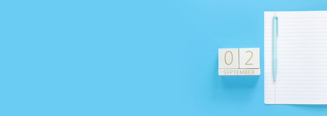 02 September. Wooden calendar on a blue background with an open notepad, top view. Back to school. Perpetual calendar, notebook and pen. Mock up