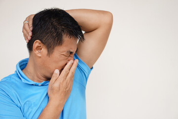 Asian man is checking his odor underarm, close his nose with hand, feel disgusted the body strong...