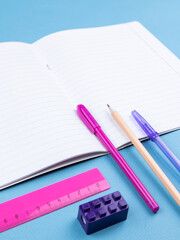 close-up of a paper notebook with blank sheets, a pen, a pencil and a paper clip on a blue background