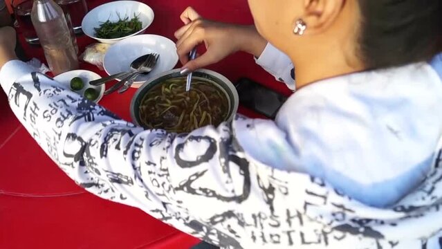 lady eating mami noodle soup along the sidewalk of a town street