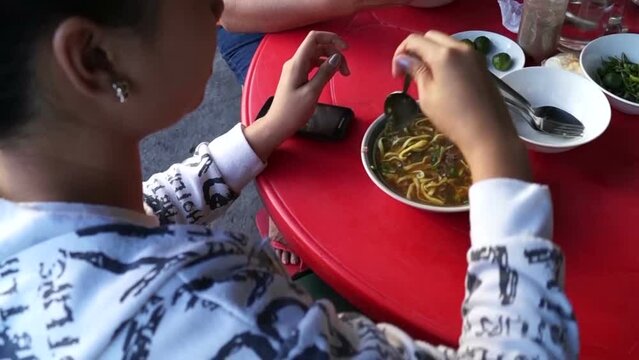 lady eating mami noodle soup along the sidewalk of a town street