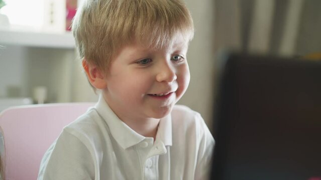 Preschooler opens mouth excitedly watching cartoon on computer. Emotional little boy smiles and licks lip reacting to action on screen closeup