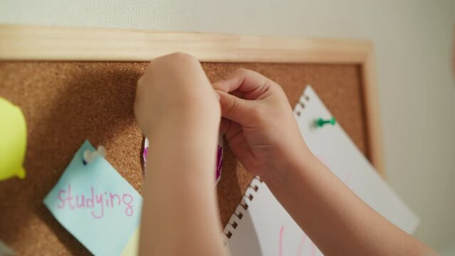 Child hands pins bright colourful picture to cork board