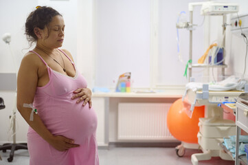 Birthing mother has contraction, holding her belly in labor room of maternity hospital. Pregnancy...