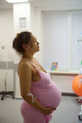 Pregnant woman, birthing mother in hospital ward, holds her belly, practices breathing exercises to...