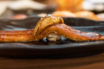 Delicious Unagi nigiri sushi (Eel Sushi) with foie gras on top on black plate. Traditional Japanese cuisine.