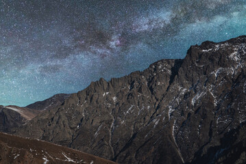Beautiful night landscape, snow covered mountains in the night. Bright milky way galaxy behind them.