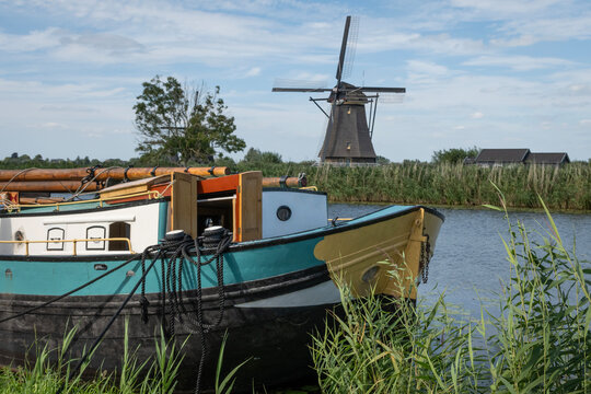 Classic Dutch scene Holland windmill in Kinderdijk with barge houseboat on canal water next to farmland polder. Netherlands rural country traditional lifestyle outdoors on sunny summer day