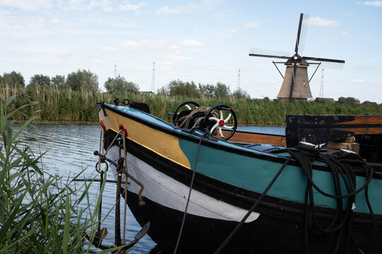 Classic Dutch scene Holland windmill in Kinderdijk with barge houseboat on canal water next to farmland polder. Netherlands rural country traditional lifestyle outdoors on sunny summer day