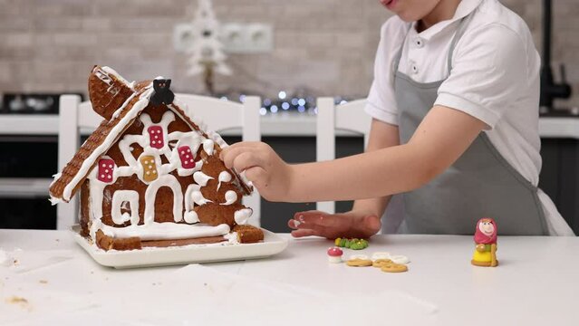 siblings boys doing with granny gingerbread christmas house.preschooler child wearing toque chef  hat,apron,mixing cream,licking from wires beaters.toddler with tree headband,modern kitchen 4k