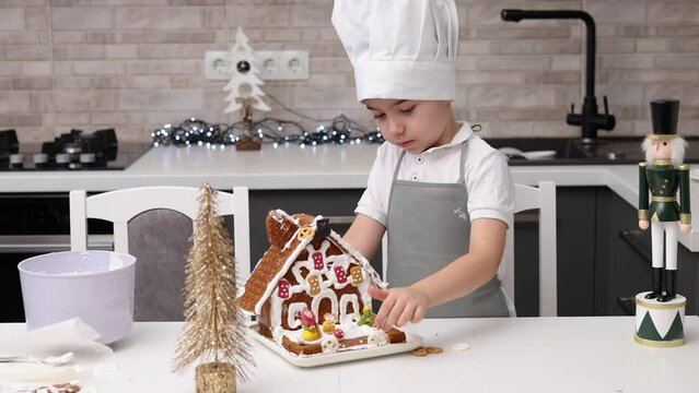 siblings boys doing with granny gingerbread christmas house.preschooler child wearing toque chef  hat,apron,mixing cream,licking from wires beaters.toddler with tree headband,modern kitchen 4k