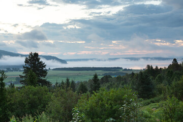 High angle view of a hill covered in trees, the Baie-Saint-Paul valley and the St. Lawrence River seen from route 138 during a beautiful foggy summer sunrise, Charlevoix, Quebec, Canada