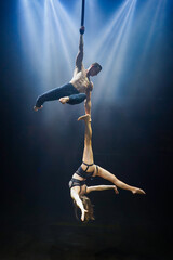  A straps duo performs an aerial act, the man holding the woman upside-down by her feet, both displaying great strength, balance, and coordination. Under dramatic blue lighting.