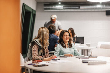 Female coworkers having fun conversation and smiling while working together at the office