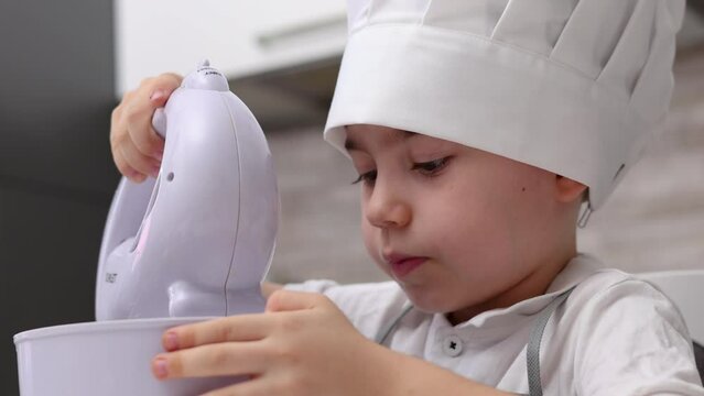 siblings boys doing with granny gingerbread christmas house.preschooler child wearing toque chef  hat,apron,mixing cream,licking from wires beaters.toddler with tree headband,modern kitchen 4k