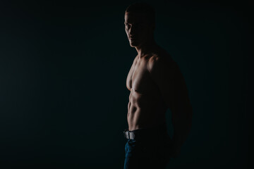 Silhouette shot of strong man showing his abs while looking away. Studio shot